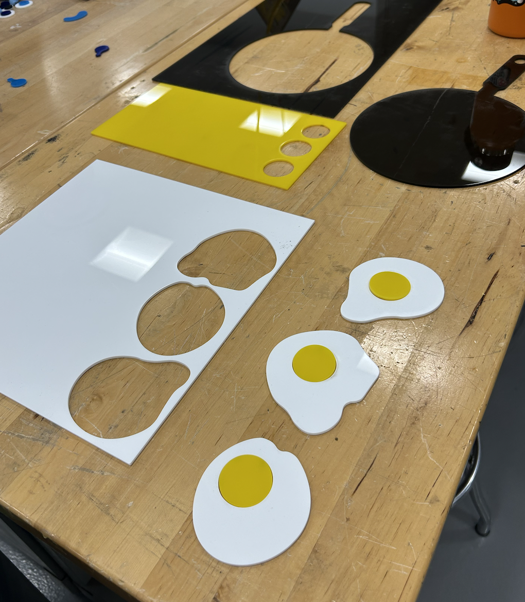 lasercut acrylic plastic on a wooden table with plastic eggs and a black plastic frying pan